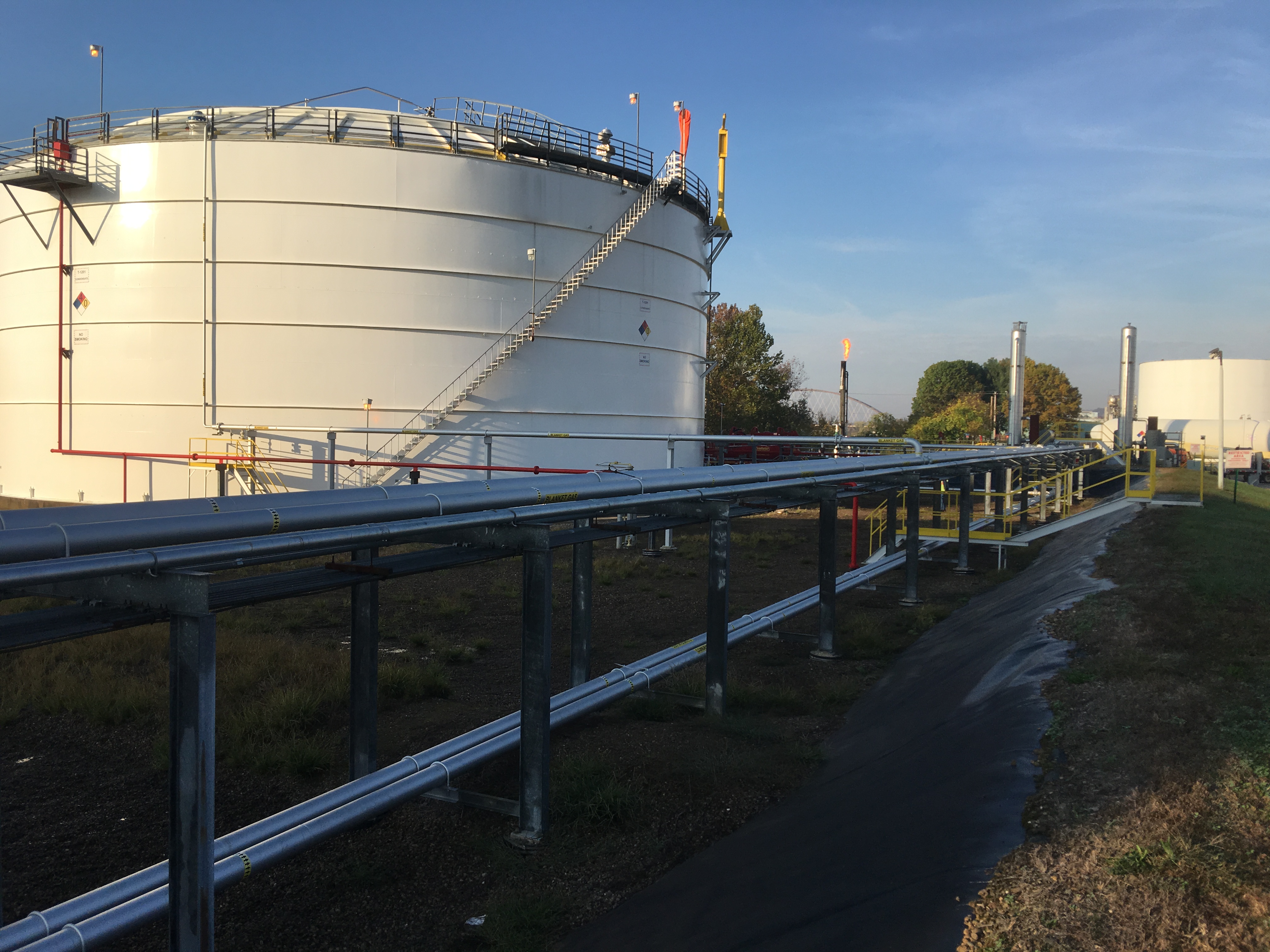 Belpre terminal at dusk — floating-roof tank and long pipe rack extending to distant tanks, warm evening light